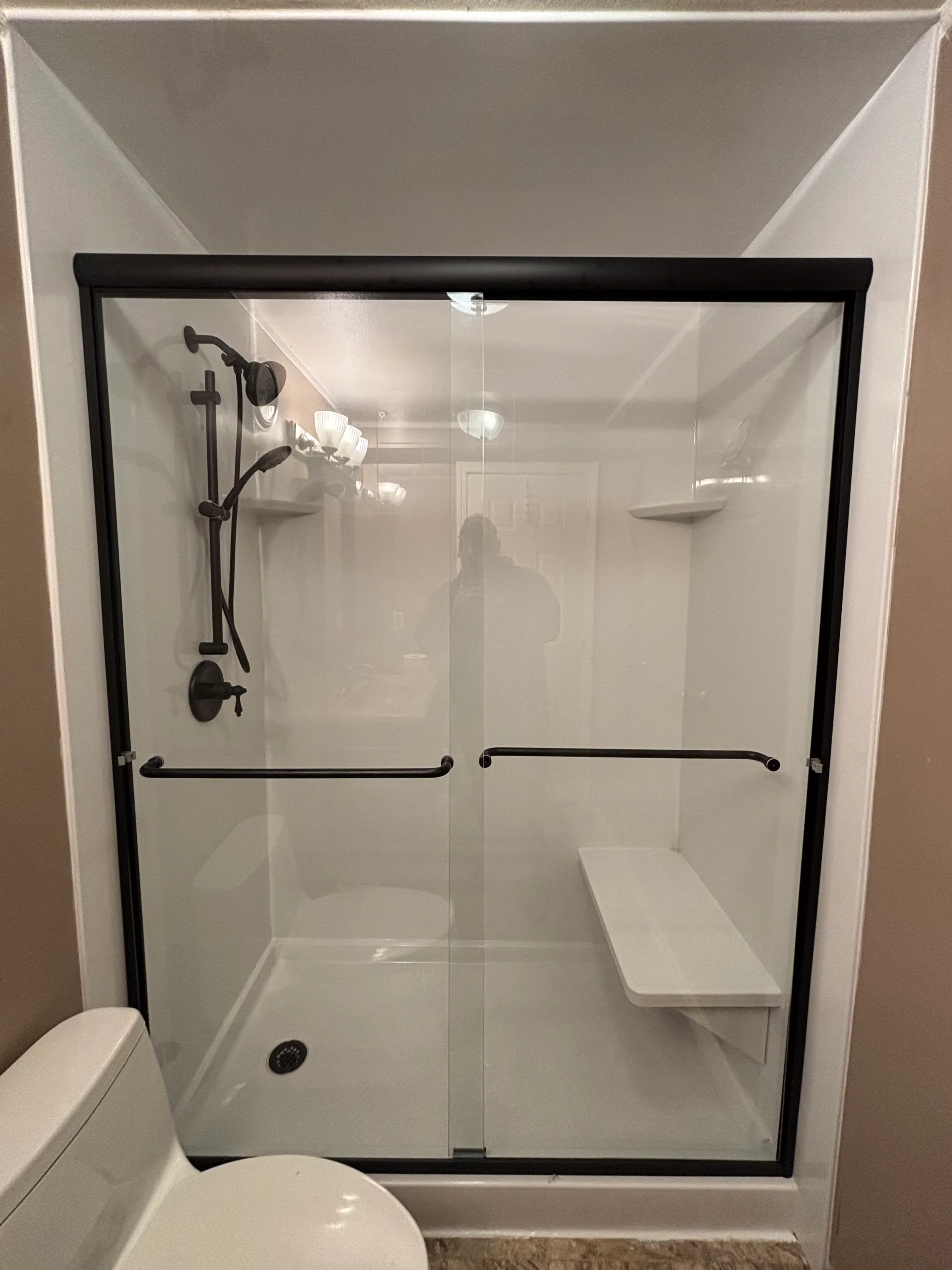 A finished acrylic shower installation in a Tacoma home bathroom, showing clean white wall panels, a low-profile base, and a polished chrome fixture against a compact single-bathroom layout. Work completed by MIDNIGHT TILE & REMODEL, LLC.