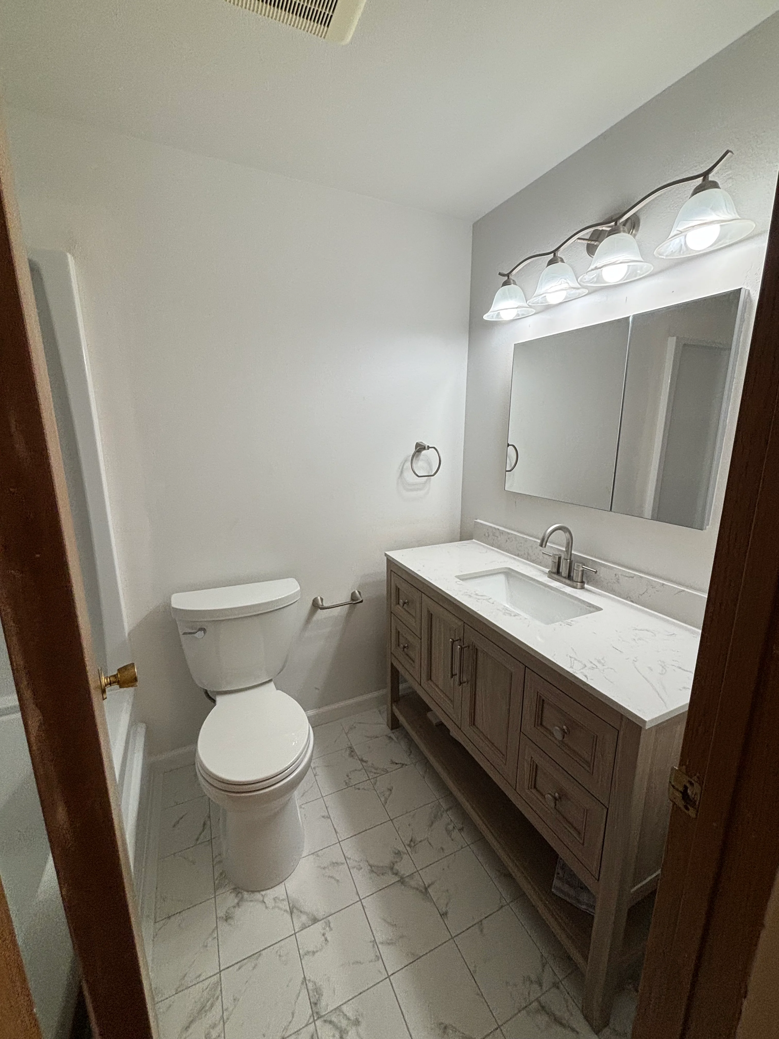 A newly installed bathroom vanity with a white cabinet base, integrated sink, and brushed hardware in a Tacoma home bathroom. The vanity is flush against a freshly caulked wall with clean plumbing connections visible beneath the cabinet.