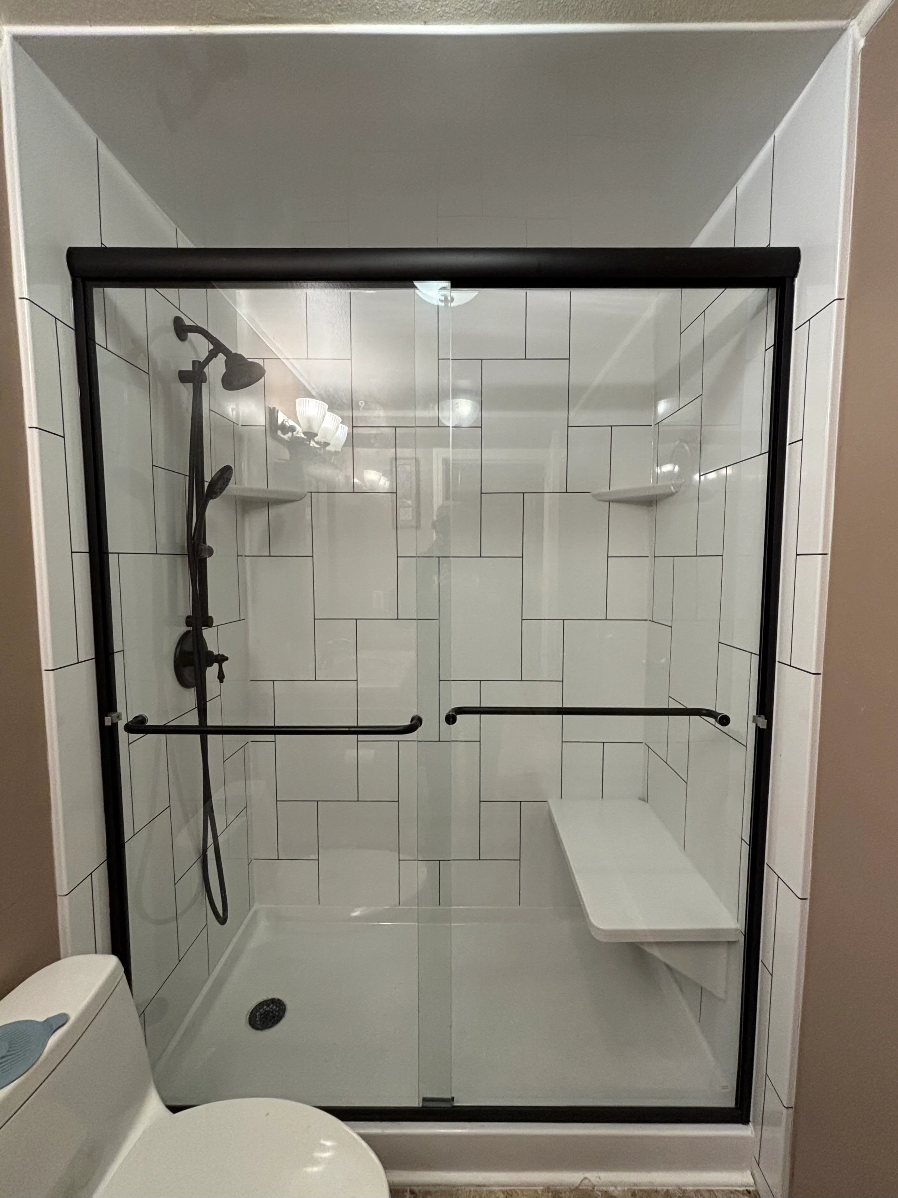 A finished custom tile shower in a Tacoma home bathroom, showing floor-to-ceiling porcelain tile, a built-in wall niche, and a frameless glass door. The shower pan and wall surfaces are fully tiled with clean grout lines and sealed joints.