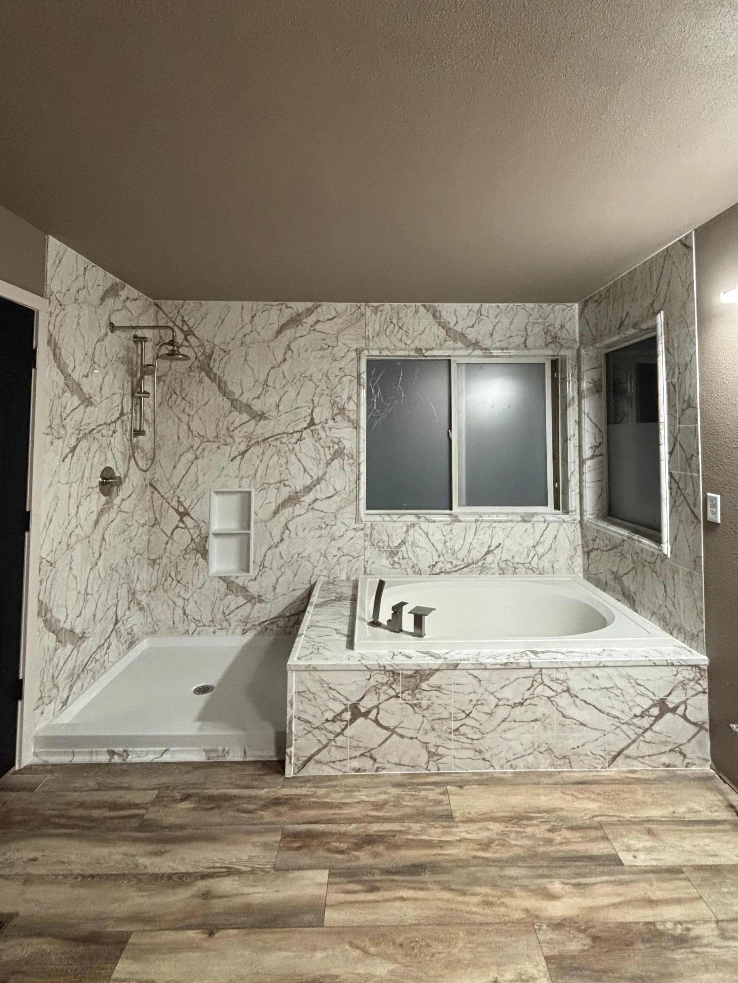 A finished tub to shower conversion in a Tacoma home, showing a fully tiled walk-in shower with a recessed wall niche and frameless glass enclosure where a standard bathtub once stood. The tile work runs floor to ceiling with clean grout lines and a low-threshold entry suited to the compact bathroom layout common in mid-century Tacoma homes.